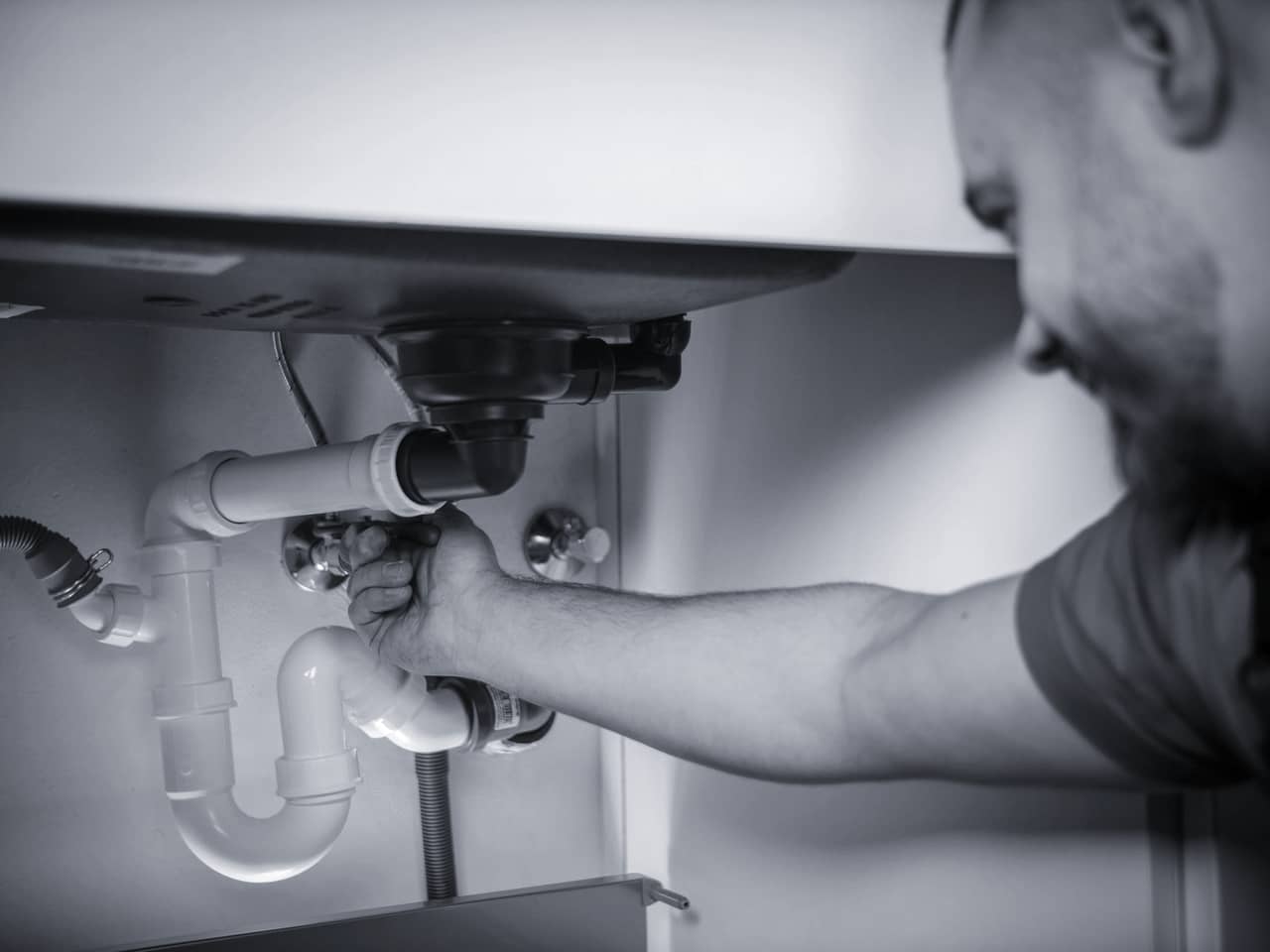 A heating engineer working on plumbing under a sink in a customer's home.